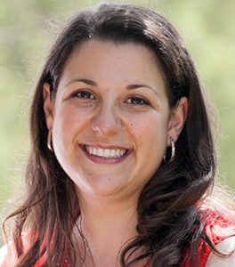 A woman smiling for the camera with trees in the background.