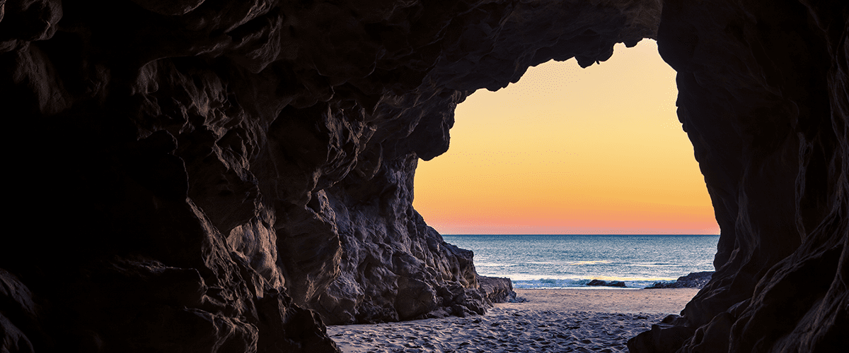 A cave on the beach with a sunset in the background.